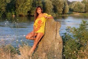 girl in a short dress near a small rock near the water