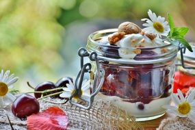 Beautiful cherry dessert with cream in a transparent jar among the colorful flowers