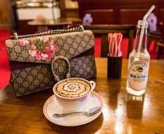 cup with coffee near a ladyâs bag