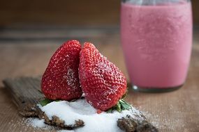 two Strawberries stands side by side in heart form in front of drink in glass