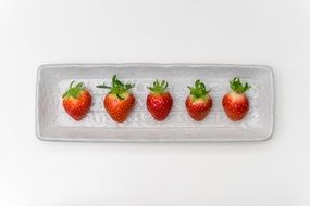 five ripe strawberries on a white plate