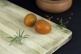 two tomatoes and rosemary branches on a wooden board in the kitchen