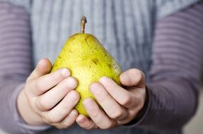 green pear in children's hands close-up on blurred background