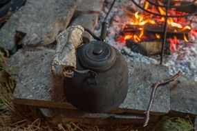 smoked teapot on stone at campfire