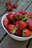 Strawberries in white bowl on wooden table