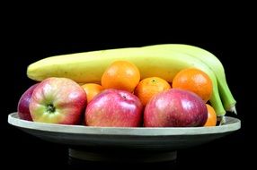 illuminated pile of fruits on plate in darkness