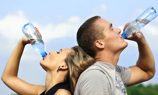 young couple drinks water from plastic bottles