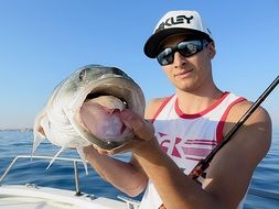 male Fisherman on boat holds big Fish