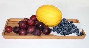 Honeydew melon and plums on a wooden board