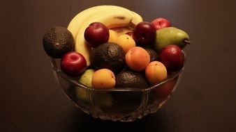 apples, apricots, bananas and avocados in a bowl