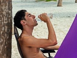 man Drinks Water on Beach