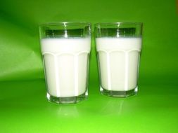 two glasses of milk on green