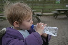 a child in a blue jacket drinks water