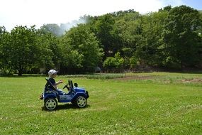 child in a kids jeep on a green lawn on a sunny day