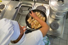 cook stands behind a stove with a frying pan