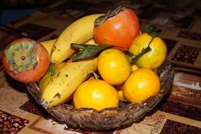 tangerines, bananas and persimmons in a transparent bowl