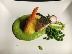 Dish made of the fish,vegetables and the green sauce on the white plate