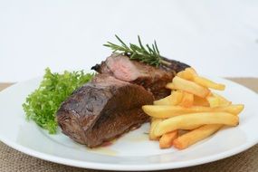 steak, french fries and greens on a white plate