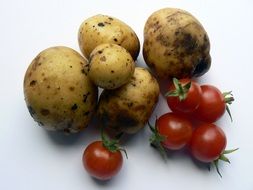 Potatoes and red tomatoes on the white surface