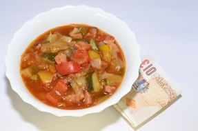 soup with vegetables and sausages and folded banknote