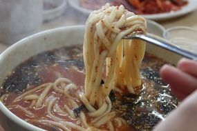 female hand with Noodles on spoon above plate