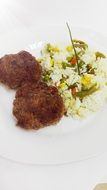 two cutlets lie on a plate with vegetable rice