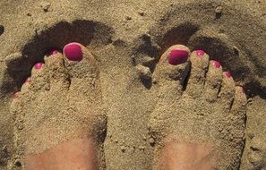 feet with a pink pedicure in the sand