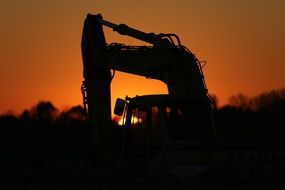silhouette of the excavator on the background of a bright sunset