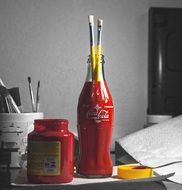 red paint in the pot and the brush in the bottle of Coca Cola