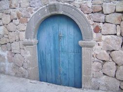 arched blue wooden door in grey stone wall, italy, Sicily