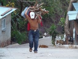 man with stack of wood on his back walks in village in Honduras