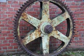 large rusty gear at brick wall