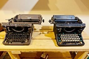two typewriters on a wooden table