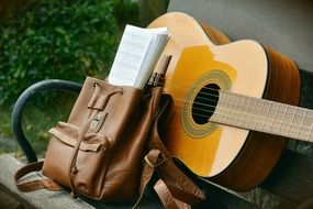 guitar and brown backpack on a bench