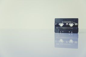 black audio cassette is reflected on the surface of the table