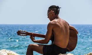 young man with guitar by the sea