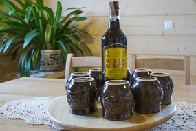 bottle of Liquor and clay mugs upside down on table