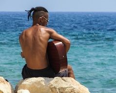 young guitar player by the sea on a sunny day