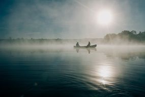 fishermen in a boat in the middle of a lake in the fog