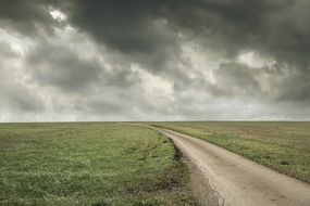 road along the fields on the background of a stormy sky