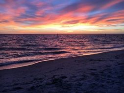 quiet waves of the ocean on the beach during colorful sunset in sky