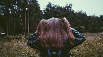 a brown-haired girl stands with her back against a dense forest