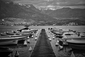 black and white photo of boats at a wooden pier on a background of mountains