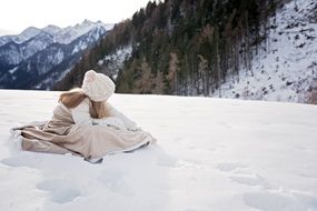 girl in a beige dress sits on a snowy mountain peak