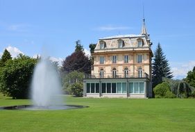 Fountain in front of a beautiful, fabulous castle on the green field near the trees