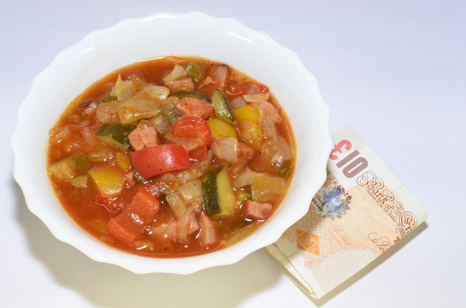 soup with vegetables and sausages and folded banknote