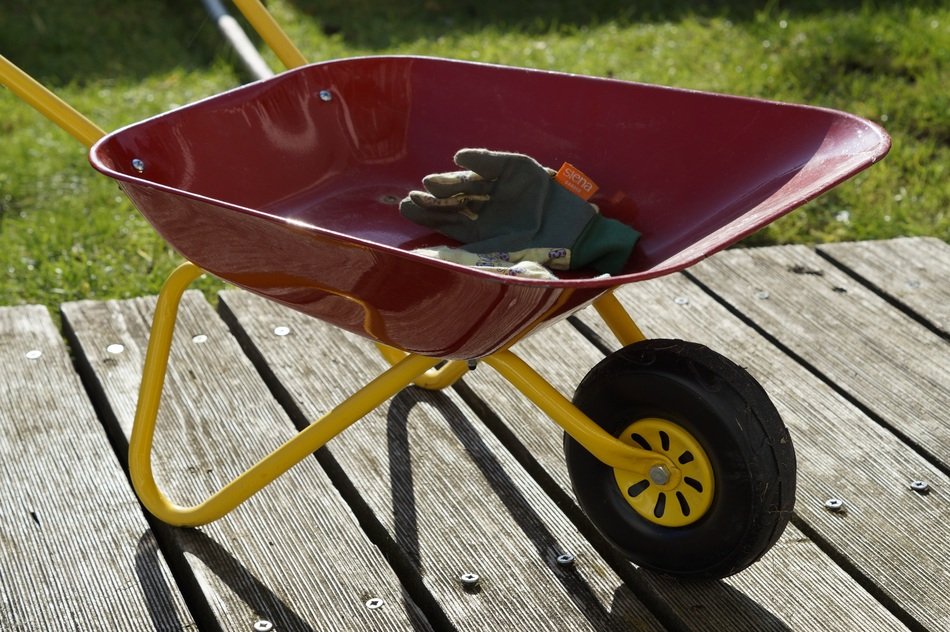 Red garden cart with working gloves on the wooden surface
