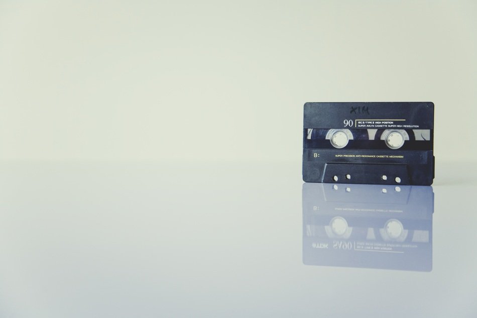 black audio cassette is reflected on the surface of the table