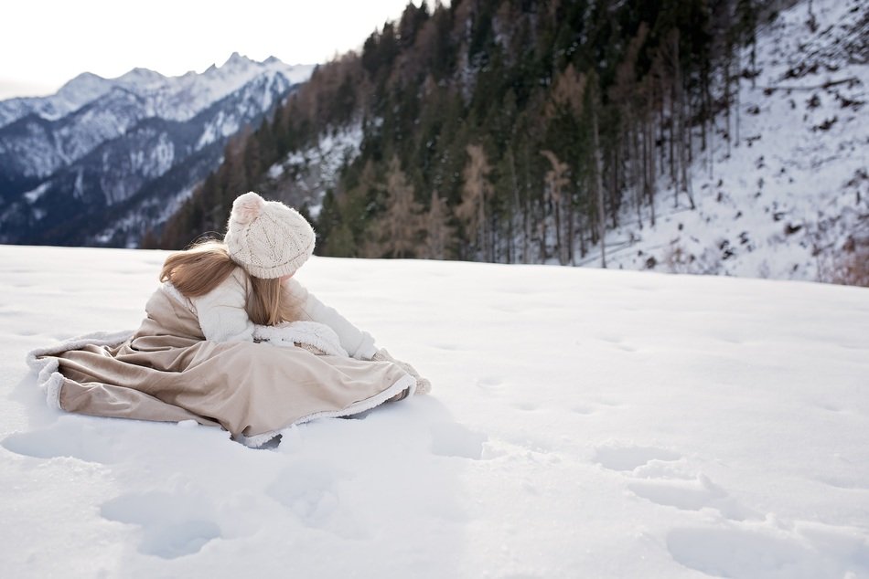 girl in a beige dress sits on a snowy mountain peak
