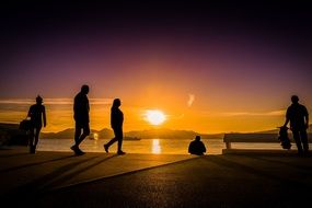 silhouettes of people walking along the seashore against the backdrop of a colorful sunset